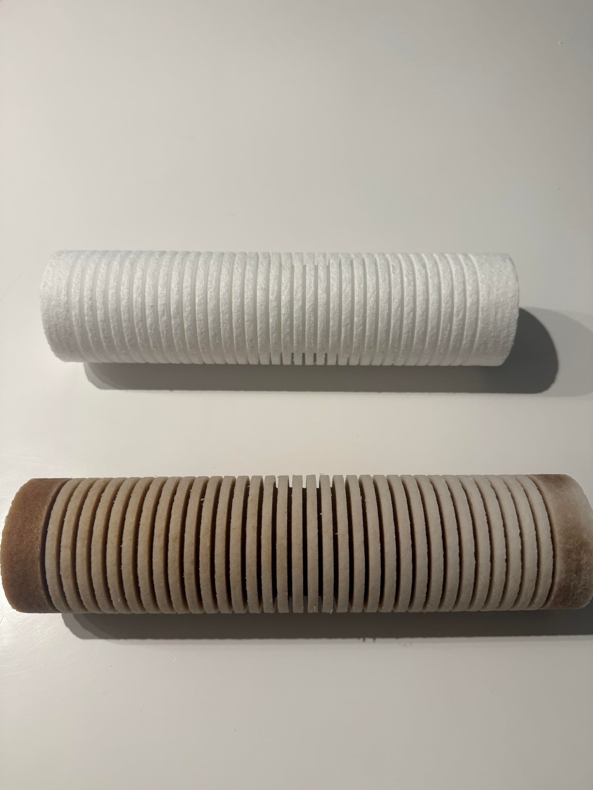 A new whole-home water filter (top) compared to the same filter after six months of use (bottom). The used filter is dark and discolored from sediment, chlorine byproducts, and other contaminants it pulled from the water.